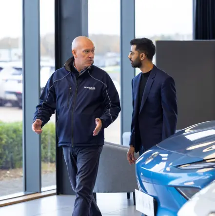 A NextGear Capital employee talking to a customer to the side of a blue car.